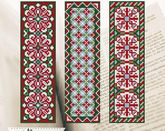 May include: Three handmade bookmarks with intricate cross-stitch patterns. The bookmarks feature red, white, green, and blue geometric designs. The bookmarks are rectangular and are displayed in front of an open book. The Etsy shop name is visible.