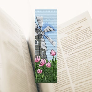 May include: A cross-stitch bookmark featuring a windmill with a blue sky and pink flowers in the foreground. The bookmark is a rectangular shape and is perfect for marking your place in a book.