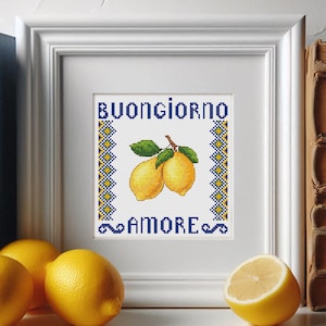 May include: A white framed cross-stitch design with a blue and yellow border. The design features two lemons on a branch with green leaves and the text "Buongiorno Amore".
