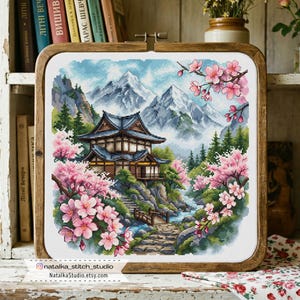 Puede incluir: Obra de arte de punto de cruz en un marco de madera que representa un paisaje japonés. La escena incluye un edificio tradicional, montañas, un río y flores de cerezo rosas. La obra está firmada por natalka_stitch_studio.