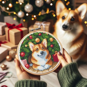 May include: A cross-stitch embroidery hoop with a colorful image of a corgi dog sitting in front of a Christmas tree. The dog is wearing a red and white sweater and has a happy expression on its face.