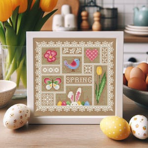 May include: A framed cross-stitch design featuring a patchwork of spring-themed images, including a butterfly, a bird, a heart, a tulip, and a bunny. The design is on a beige background with white stitching and the word "SPRING" in the center.