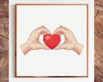 May include: Two hands forming a heart shape with a red heart in the center. The hands are stitched in a cross-stitch pattern.