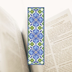 Op de afbeelding: Een kruissteek-bladwijzer met een herhalend patroon van blauwe bloemen met gele centra en groene bladeren op een witte achtergrond.