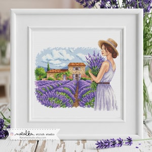 Könnte beinhalten: Gerahmte Kreuzstich-Stickerei, die eine Frau in einem Lavendelfeld mit einem Blumenstrauß zeigt. Die Szene umfasst ein Steinhaus, Lavendelreihen und einen blauen Himmel mit Wolken. NatalkaStudio.etsy.com.