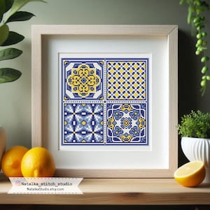 Puede incluir: Obra de arte de punto de cruz enmarcada con cuatro paneles cuadrados con patrones geométricos en azul y amarillo. La obra de arte está en un marco de madera clara y descansa sobre una superficie de madera. De Natalka Stitch Studio.