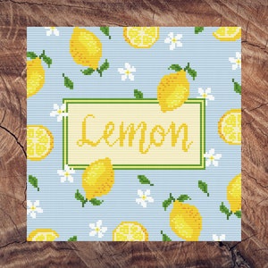 Puede incluir: Un patrón de punto de cruz azul y blanco con limones y flores blancas. El patrón incluye la palabra "Lemon" en una pancarta amarilla.