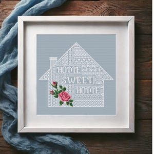 May include: White cross-stitch embroidery of a house with the words "Home Sweet Home" and a pink rose. The embroidery is framed in a white frame.