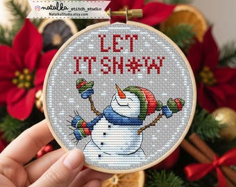 May include: A cross-stitch embroidery hoop featuring a snowman with a carrot nose, wearing a hat, scarf, and mittens. The text "LET IT SNOW" is stitched in red. The background is gray.