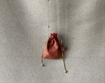 Amulet bag to wear as a long pendant necklace in coral-colored silk and golden beads.