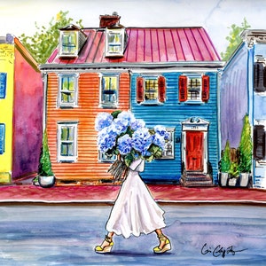 May include: A woman in a white dress walks down a street carrying a bouquet of blue hydrangeas. The street is lined with colorful houses, including a red-roofed house with a blue door.