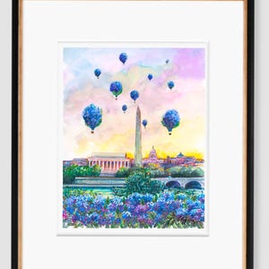 May include: Watercolor painting of the Washington Monument in Washington, D.C. with blue hot air balloons floating in the sky above the city. The painting features a vibrant sunset with pink, orange, and yellow hues. The monument is surrounded by lush green trees and a river.