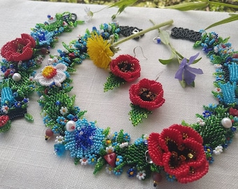 May include: A beaded necklace and earrings set featuring red poppies, blue forget-me-nots, white daisies, and green leaves. The necklace is a long, delicate chain with a floral design. The earrings are small and dangle.