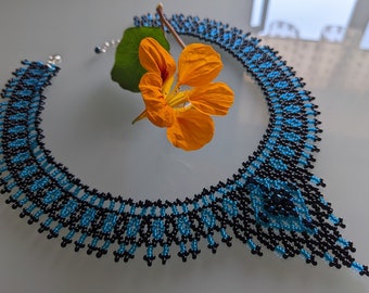 May include: A black and blue beaded necklace with a geometric pattern. The necklace is made of small beads and has a pointed, teardrop shape.