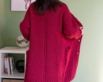 May include: A long, burgundy cardigan with pockets and a button closure. The cardigan is made of a soft, knit fabric.