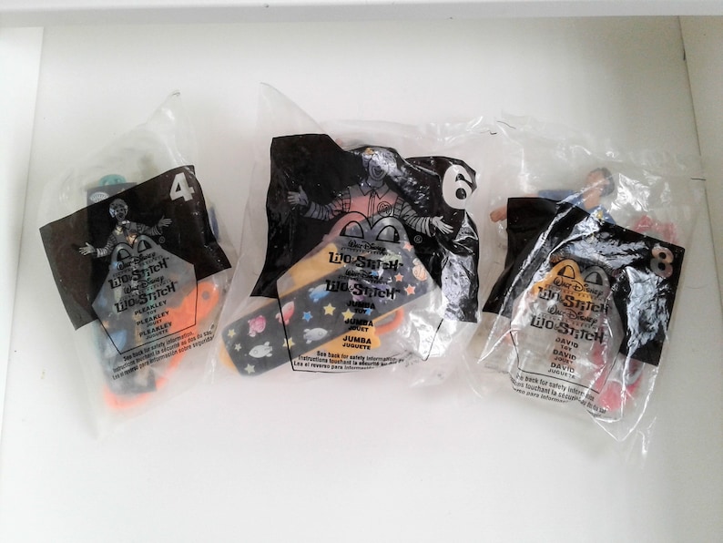 May include: Three plastic bags containing Lilo & Stitch character toys. The bags are labelled with the character's name and number. The characters are Pleakley, Jumba, and David.