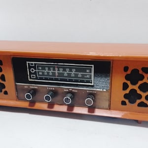 May include: A vintage wooden AM/FM radio with a brown wood cabinet, black speaker grilles, and a silver faceplate with tuning knobs. The radio has a dial with numbers for AM and FM frequencies.
