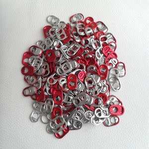 May include: A large pile of silver and red pull tabs from aluminium beverage cans. The pull tabs are arranged in a random pattern.