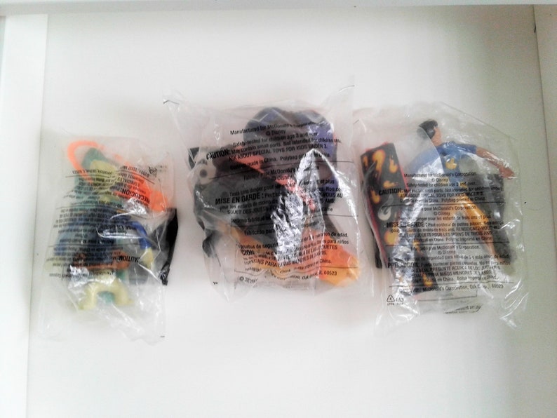 May include: Three plastic bags containing small toys. The toys are in various colours, including orange, yellow, blue, green, and black. The bags have warning labels in English and French.