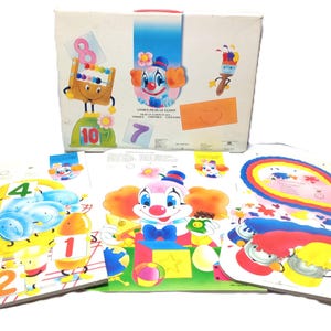 May include: A white rectangular box featuring a colourful clown illustration and the text "LIVRES POUR LE CLOWN" alongside three large activity sheets. The sheets display vibrant graphics of clowns, numbers, paintbrushes, and rainbow patterns.