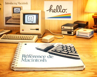 Könnte beinhalten: Ein beigefarbener Vintage-Macintosh-Computer mit einem lächelnden Gesichtssymbol auf dem Bildschirm, einer Tastatur und einer Maus. Ein spiralgebundenes Handbuch mit dem Titel Référence de Macintosh liegt im Vordergrund mit einer Abbildung.