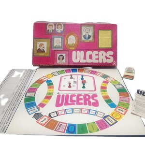 Puede incluir: Juego de mesa vintage titulado "ULCERS" con una caja rosa con retratos enmarcados. El tablero del juego es circular con espacios coloridos y el título del juego en letras rosas grandes. Incluye piezas e instrucciones.