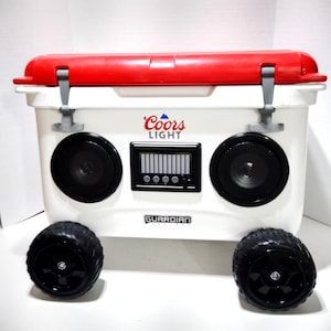 Könnte beinhalten: Weißer Kühlbox mit rotem Deckel und schwarzen Rädern. Er hat ein Coors Light Logo und ein eingebautes Boombox mit Lautsprechern. Die Kühlbox ist mit "Guardian" beschriftet.