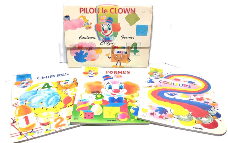 May include: A set of educational materials titled PILOU le CLOWN featuring a storage folder and three books labelled CHIFFRES, FORMES, and COULEURS. The items display colourful illustrations of a clown, geometric shapes, numbers, and rainbows.