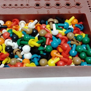 May include: A brown plastic pegboard filled with colorful mushroom-shaped pegs. The pegs are various colors, including red, yellow, green, blue, white, and brown. The pegboard has holes for the pegs and is a classic educational toy.