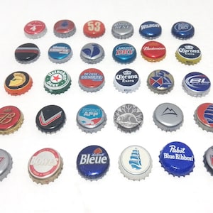 May include: A collection of 28 bottle caps featuring various logos and designs, including Corona Extra, Budweiser, Heineken, Molson Dry, and Wildcat. The caps are arranged in a grid pattern on a white background.