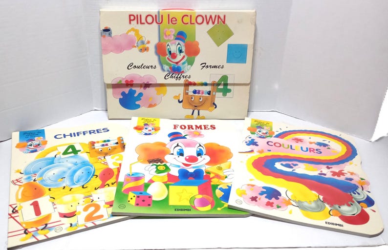 May include: A set of educational materials titled PILOU le CLOWN, including a storage folder and three books labelled CHIFFRES, FORMES, and COULEURS. The items feature colourful illustrations of a clown, numbers, geometric shapes, and rainbows.