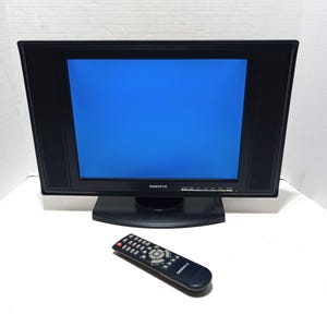 May include: A black Daenyx television with a bright blue screen and integrated side speakers, featuring a matching black remote control with numerous buttons and the Daenyx brand name printed on both the television frame and the remote.
