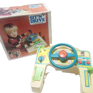 Puede incluir: Juguete vintage Fisher-Price Sit 'N Drive. El juguete tiene un volante, palanca de cambios y controles del tablero en azul, rojo, amarillo y verde. La caja muestra a un niño jugando con el juguete. El texto "SIT 'N DRIVE" es visible.