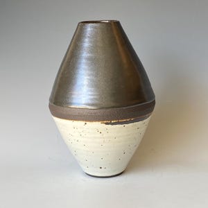 Könnte beinhalten: Eine Keramikvase mit konischer, geometrischer Silhouette. Der obere Teil ist mit einer glatten, glänzenden dunkelbraunen Metallic-Glasur versehen, während der untere Bereich ein mattes, cremefarbenes Finish mit Sprenkeln und Rillen aufweist.
