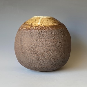 Op de afbeelding: Een ronde keramische vaas met een getextureerd bruin exterieur en een lichtbruine en witte rand.