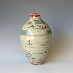 Könnte beinhalten: Eine Keramikvase mit verjüngtem Hals und bauchigem Körper, die eine cremefarbene Glasur mit horizontalen Bändern aufweist. Die Oberfläche ist mit handgemalten schwarzen Tuschezeichnungen von ländlichen Landschaften, Bäumen und Gebäuden verziert.