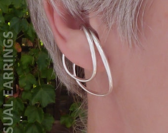 May include: A pair of silver ear cuffs, one slightly larger than the other, worn on the upper lobe of an ear.