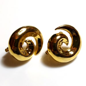 May include: A pair of gold-tone earrings with a spiral design. The earrings are made of a smooth, shiny metal.