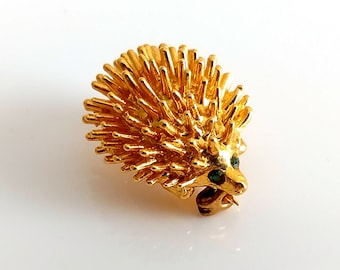 May include: A gold-toned brooch in the shape of a hedgehog with green gemstone eyes.