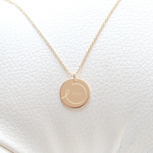 Peut inclure: Collier en or avec un pendentif rond orné d'un ruban blanc, inscrit du mot "Hope".