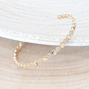 Könnte beinhalten: Ein goldenes Armreif-Armband mit einer Reihe kleiner, runder, pavé-besetzter Steine.