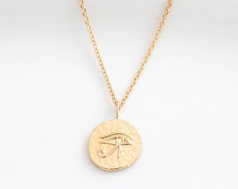 May include: A gold chain necklace with a round pendant featuring an embossed eye of Horus symbol.