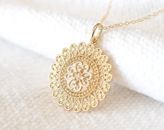 May include: A gold necklace with a delicate, circular pendant featuring a floral design. The pendant is intricately detailed and has a filigree pattern.
