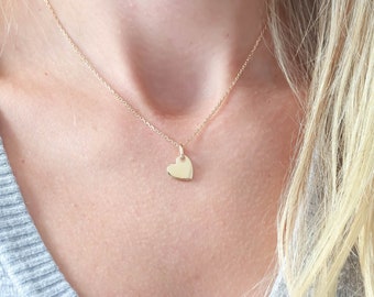 May include: A gold heart pendant necklace on a person's chest. The necklace is thin and delicate, and the heart pendant is small and simple.