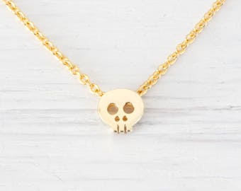Könnte beinhalten: Eine goldene Kettenkette mit einem kleinen, goldenen Totenkopf-Anhänger.