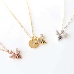 May include: Three gold necklaces with bee charms. The bee charms are adorned with small clear stones. One necklace has a round pendant with the letter "F" engraved on it.