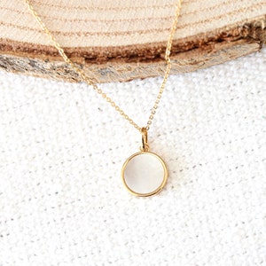May include: A gold chain necklace with a round, white pendant. The pendant has a smooth, polished surface.