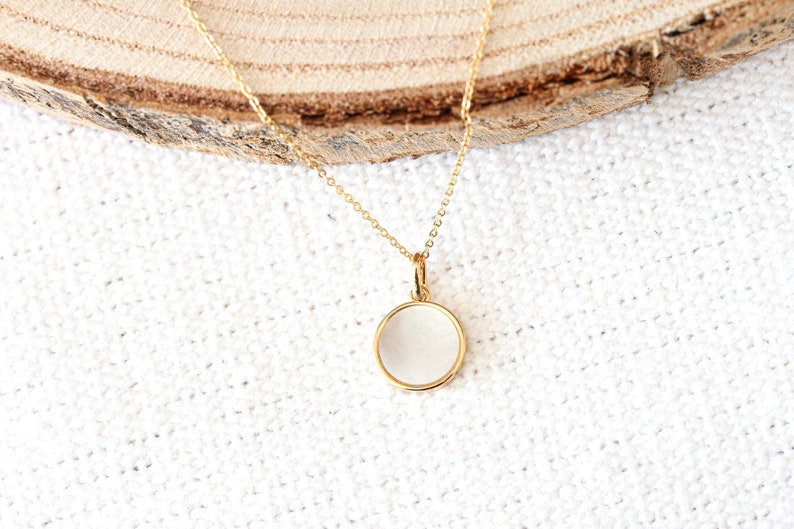 May include: A gold chain necklace with a round, white pendant. The pendant has a smooth, polished surface.