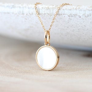 May include: A gold chain necklace with a round, white mother-of-pearl pendant.