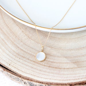 May include: A gold chain necklace with a white round pendant. The pendant is made of mother of pearl and has a gold rim.